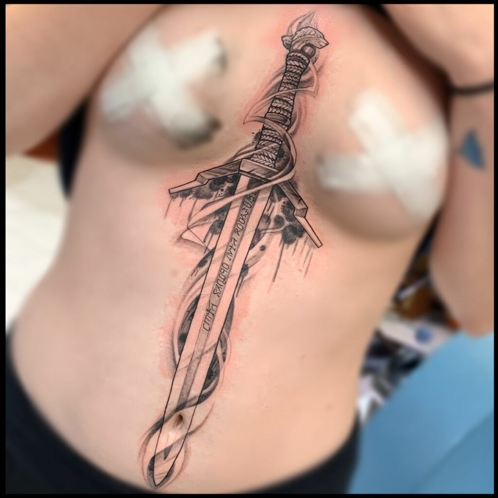 Sword upper body in between breast tattoo